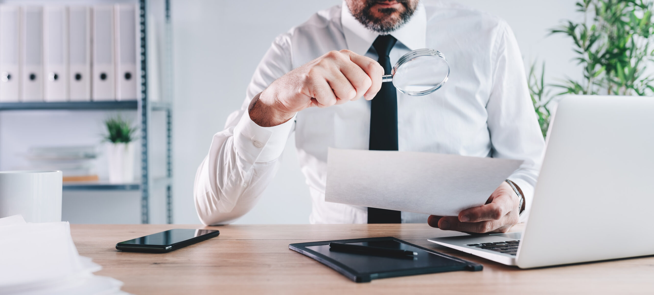 Tax inspector and financial auditor looking through magnifying glass, inspecting financial papers