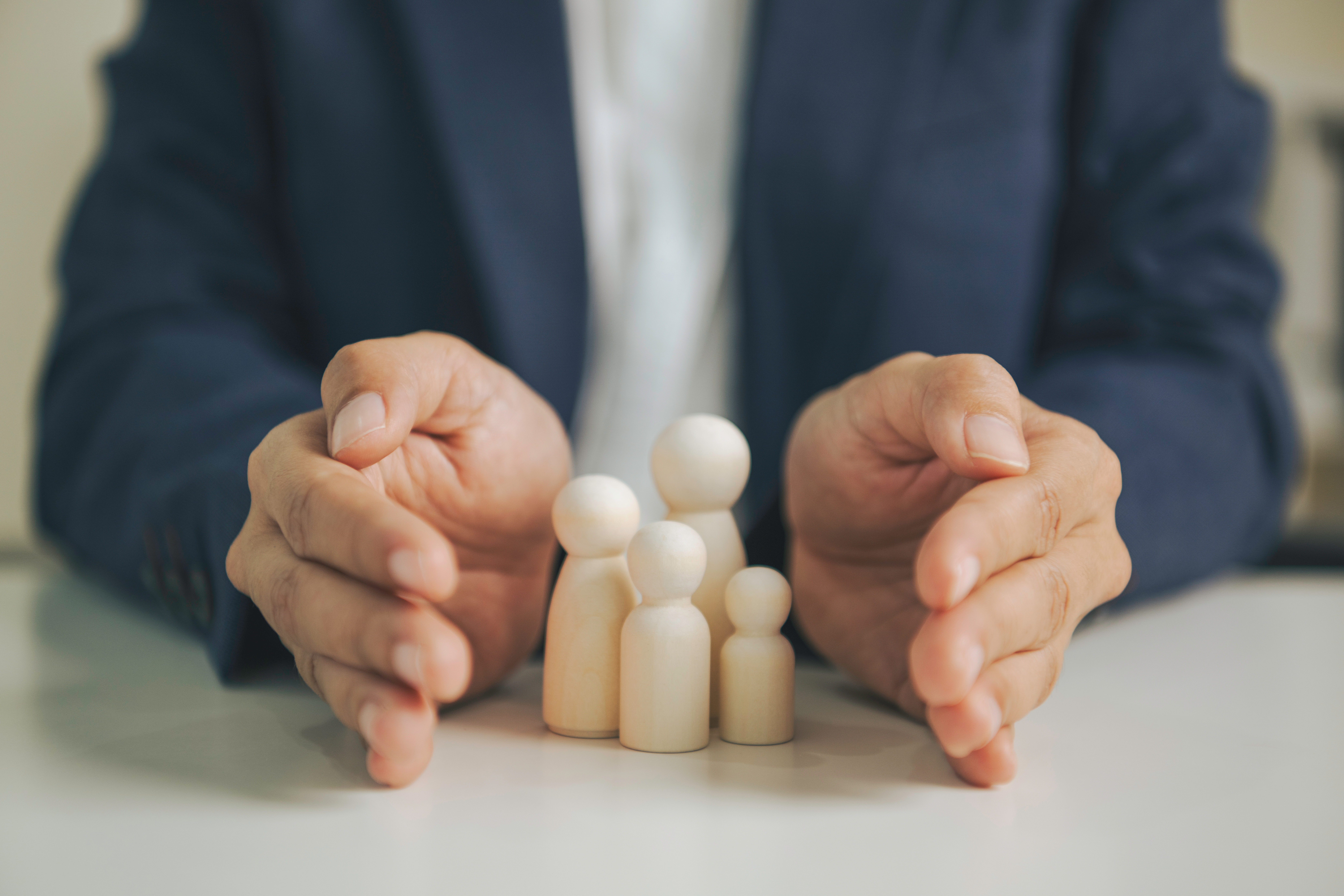 Family financial protection concept with wooden figures and advisor hands demonstrating insurance planning risk management wealth security and long term household stability